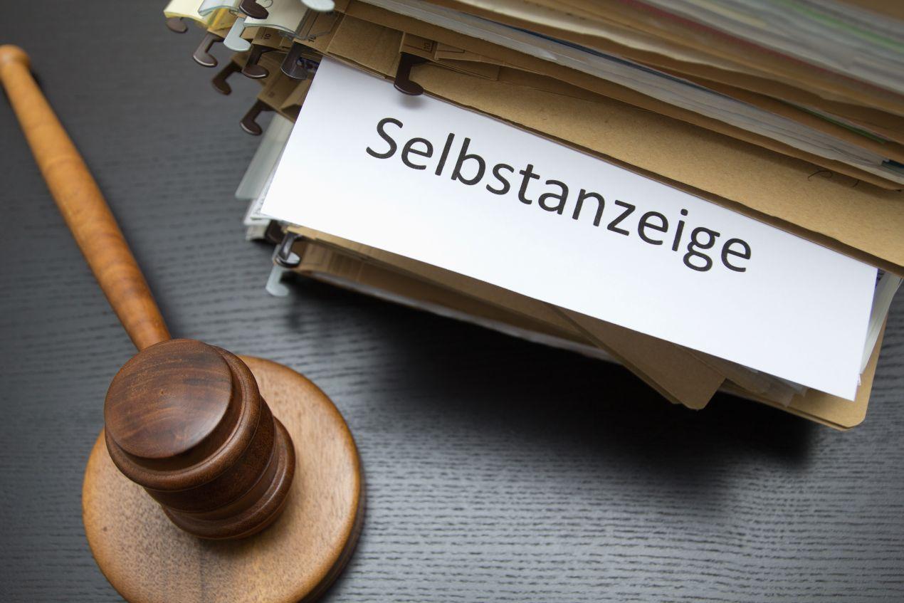 Ein Aktenordner mit dem Schriftzug „Selbstanzeige“ und ein Richterhammer – Symbol für rechtliche Konsequenzen bei Steuerhinterziehung.