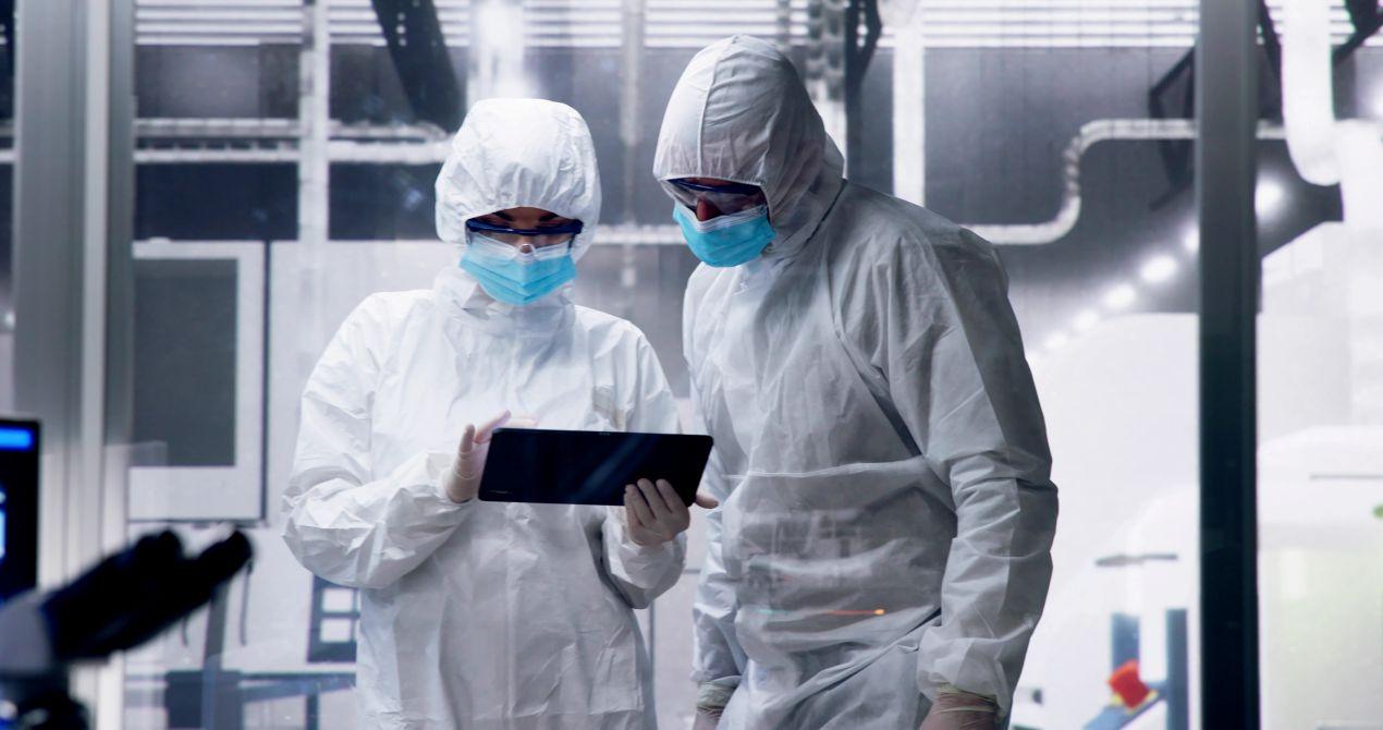 Zwei Mitarbeitende im Reinraum mit Schutzkleidung dokumentieren Reinigung digital per Tablet