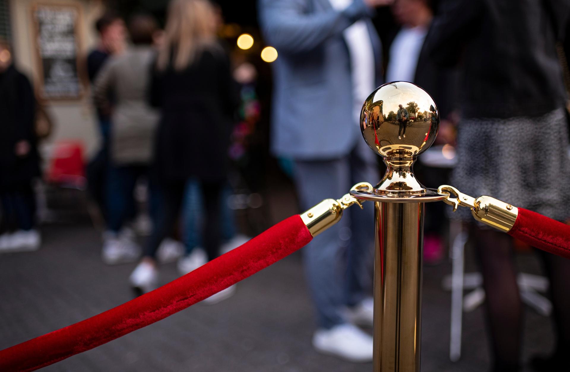 Goldene Pfosten mit rotem Band vor Gästen | Personenleitsystem