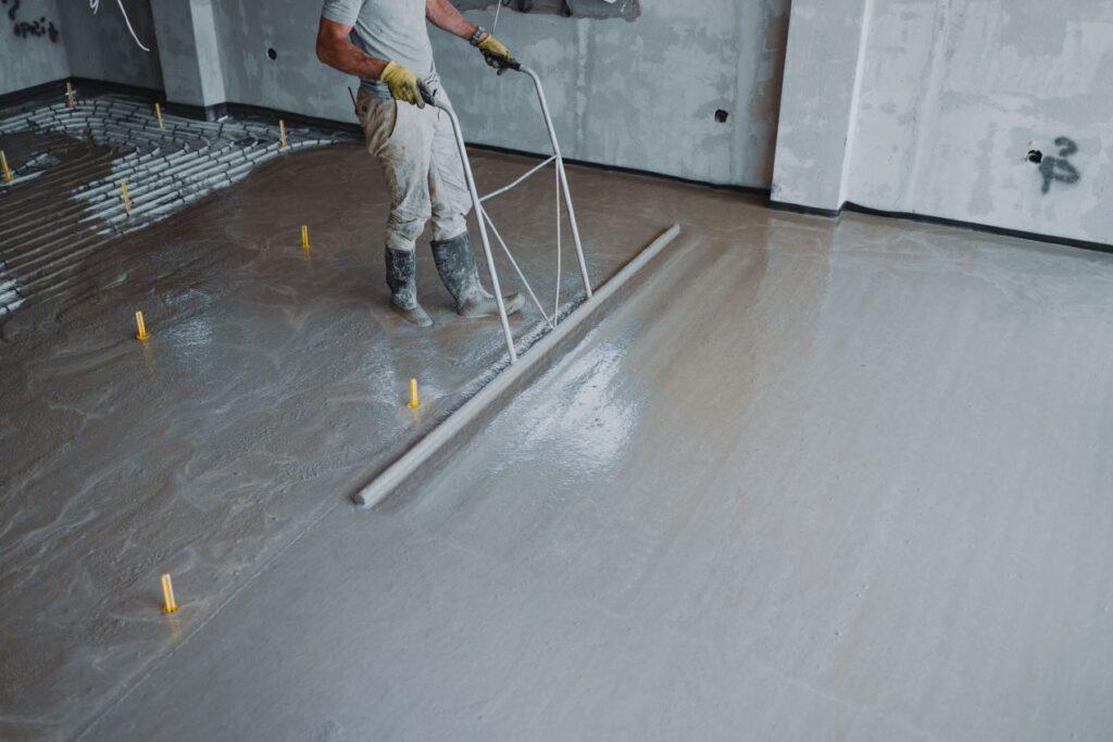 Handwerker glättet frischen Betonboden in modernem Neubau, befestigt mit Betonschrauben fuer maximale Stabilitaet und Praezision.